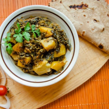 Aloo palak served in a bowl with roti, fresh salad and raita.