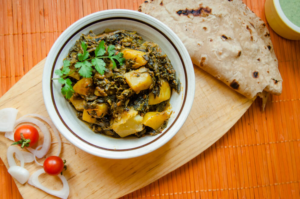 Delicious aloo palak served in a bowl with roti, raita and salad.