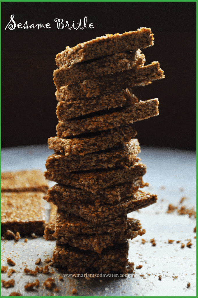 A pile of thin til chikki standing over the metal tray.