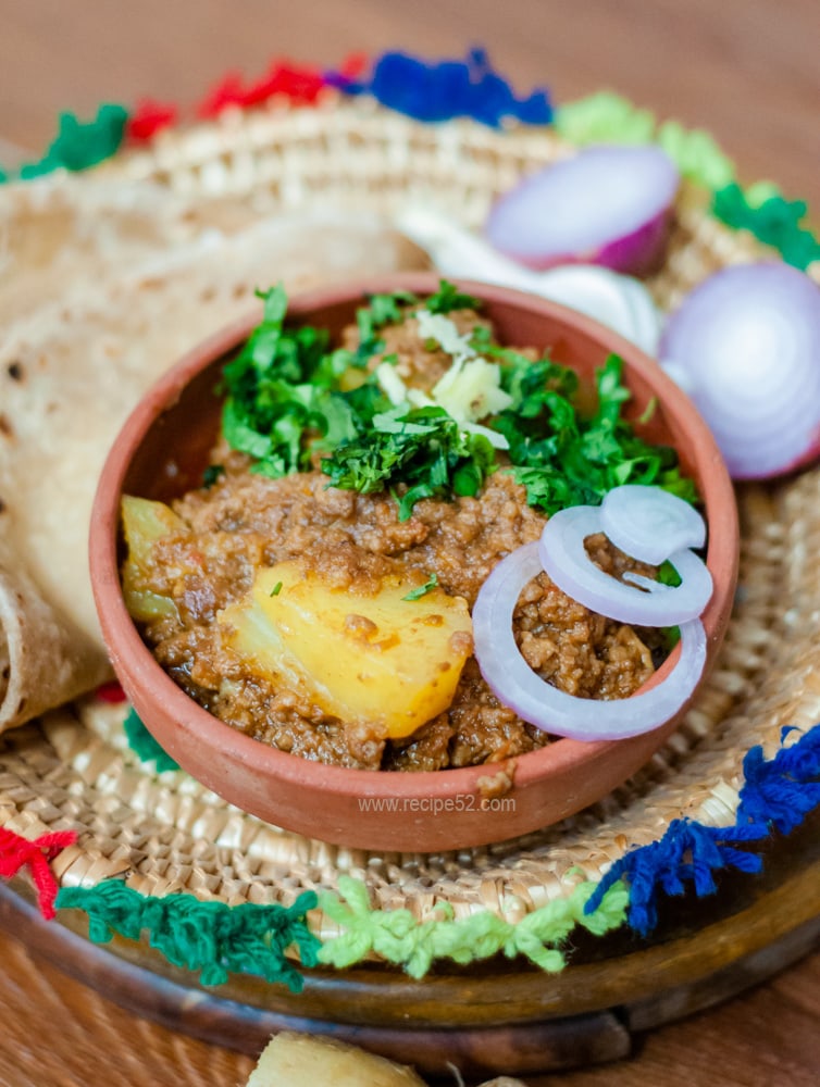 Aloo keema, ground beef and potato curry served in a clay bowl with cilantro and ginger garnish.
