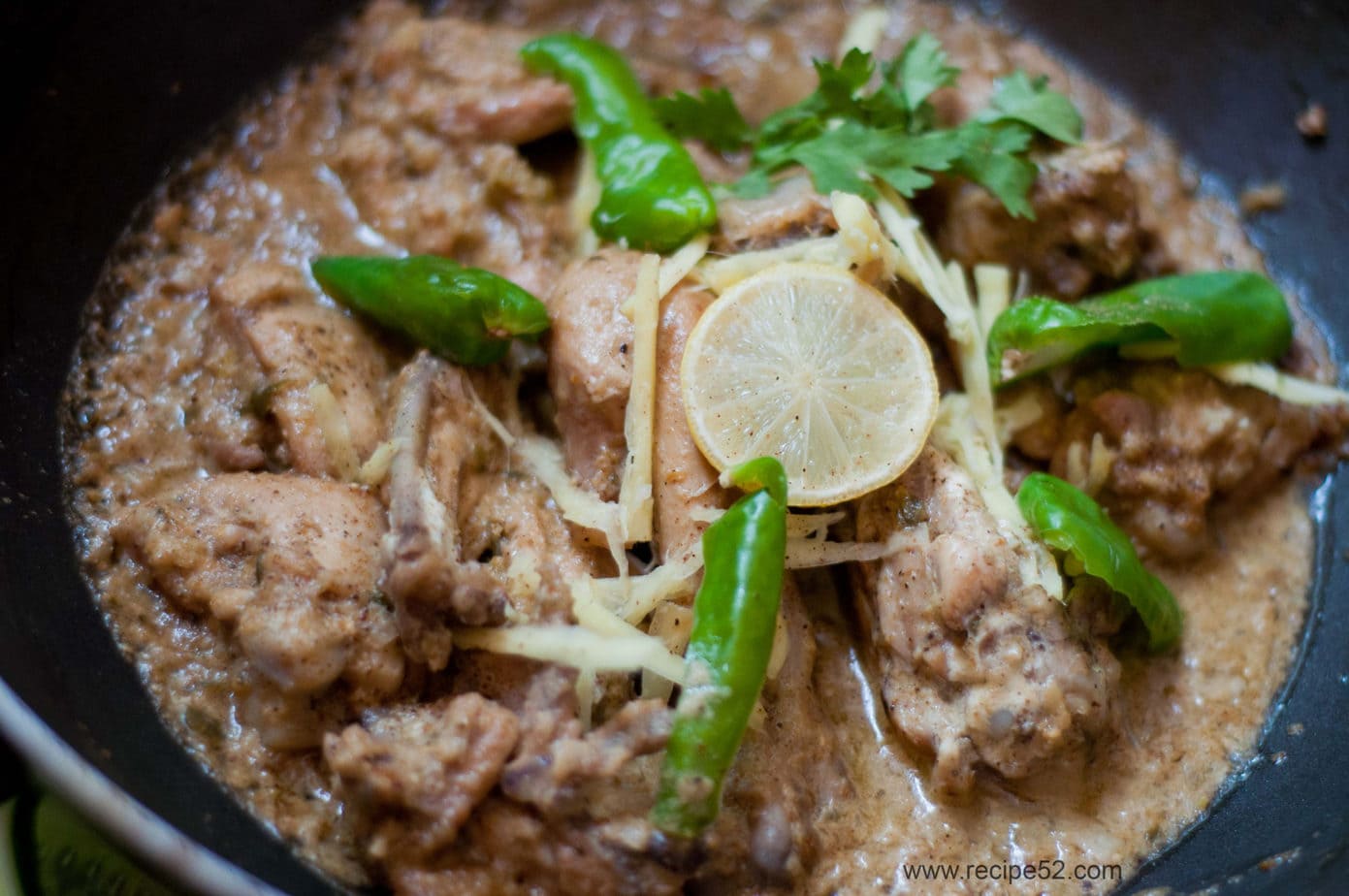 A close up shot of chicken white karahi garnished with green chillies and a slice of lemon.