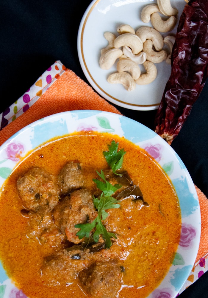 meatballs curry served in blur floral plate with cashew and chili on the side,