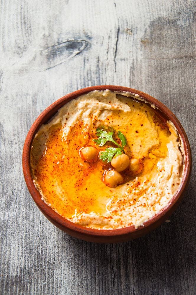 Hummus in earthern bowl with olive oil, Chickpea and paprika garnish.