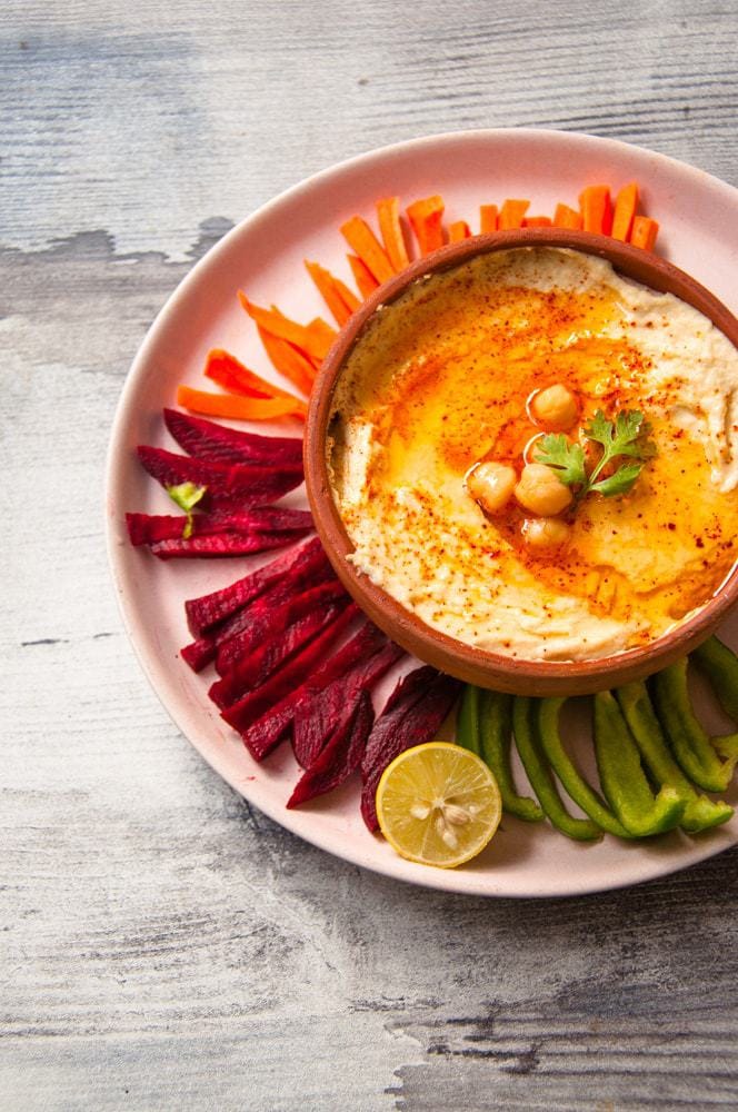 Hummus served in plate with veggies strip to dip in the sauce.