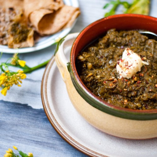 sarson saag or Indian Pakistani mustard greens served in a pot with a dallop of butter melting over it.
