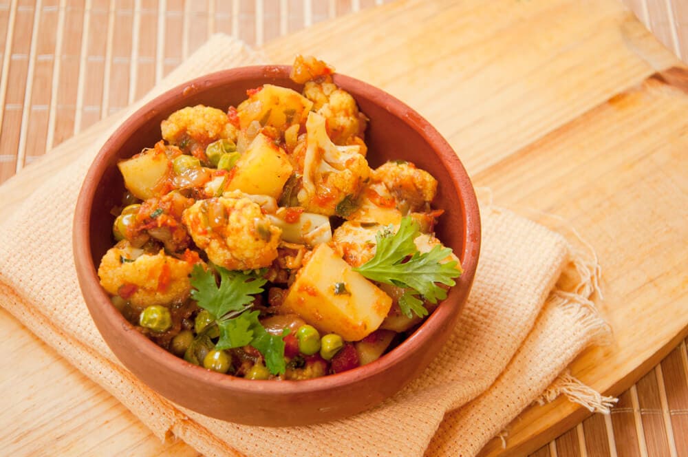 aloo gobi matar served in a clay bowl over yellow cloth.