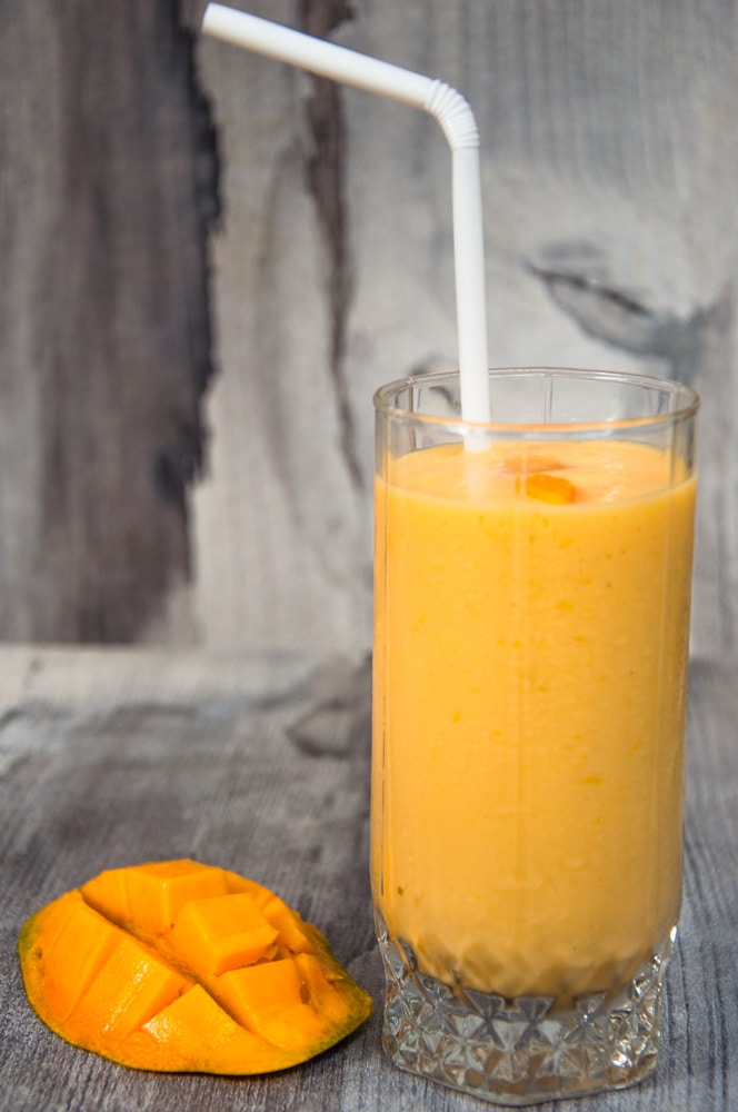 Mango milkshake served in a glass with straw in it.