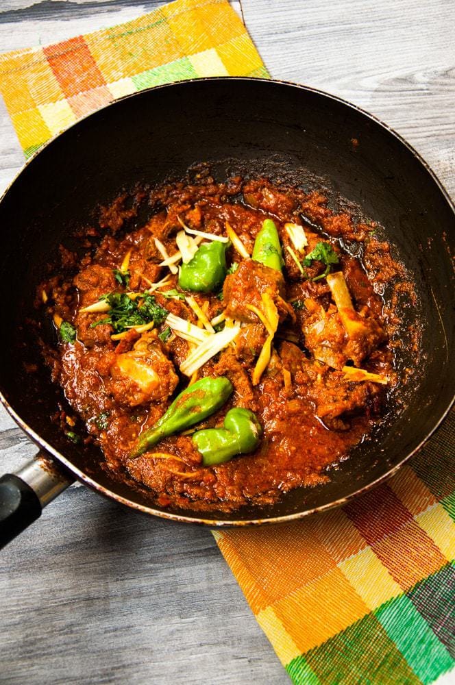 Lamb Karahi kept on colourful spread with chili and ginger garnish.