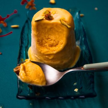 mango kulfi in kept in a plate with a kulfi bite in a spoon.