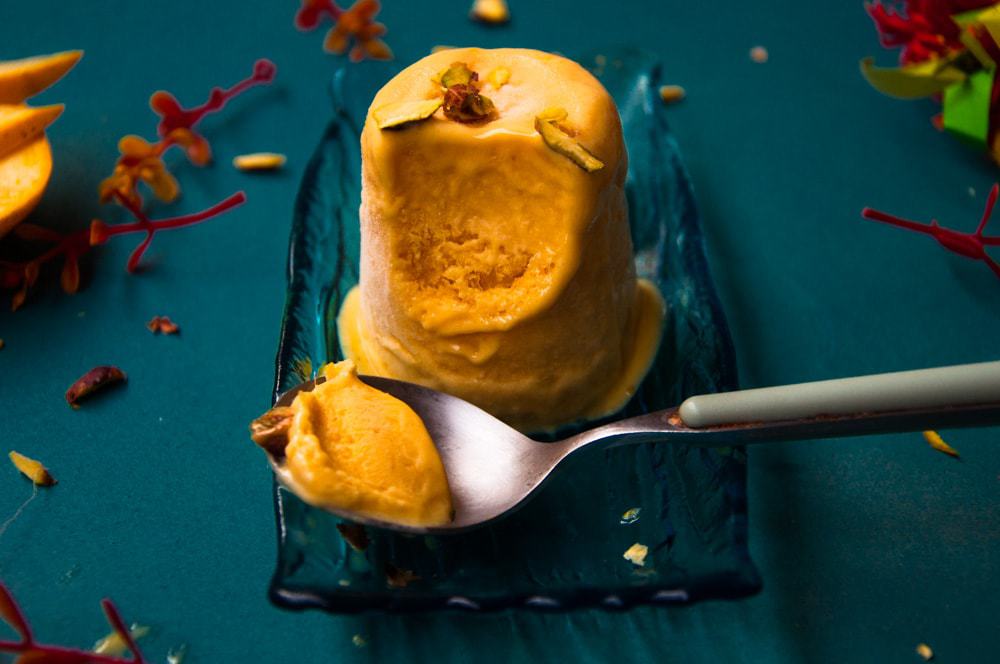 Indian dessert in kept in a plate with a bite in a spoon.