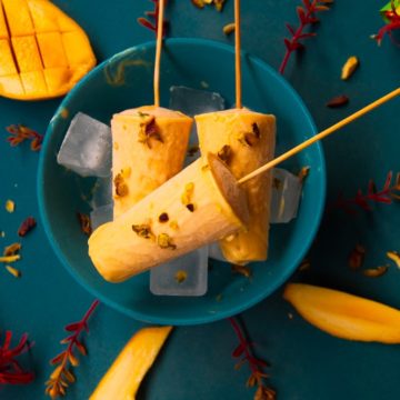 Mango kulfi in a bowl over ice cubes with mango slice on a side.