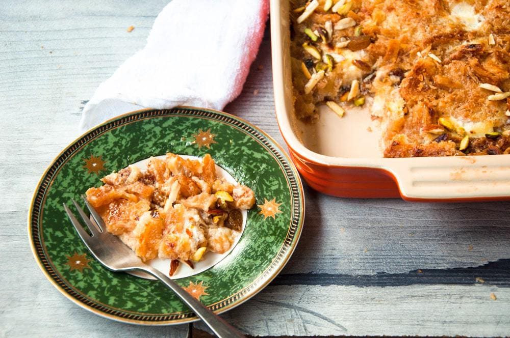 Om Ali, the Egyptian dessert is served in a plate with a spoon on the side and casserole in the background.