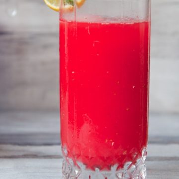 Refreshing red drink in a glass with lemon slice and mint leaf on the brim.
