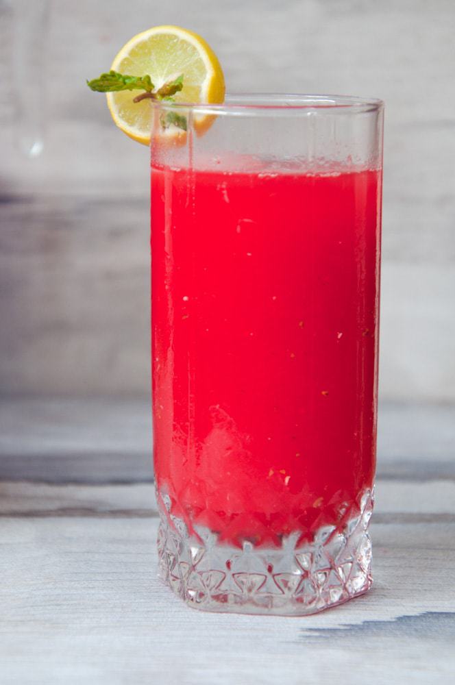 Refreshing red drink in a glass with lemon slice and mint leaf on the brim.