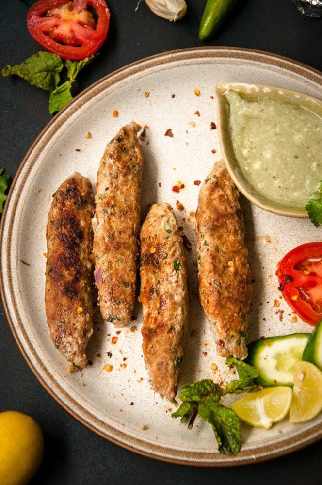 Seekh kebab served on a plate with chutney and salads on the side.