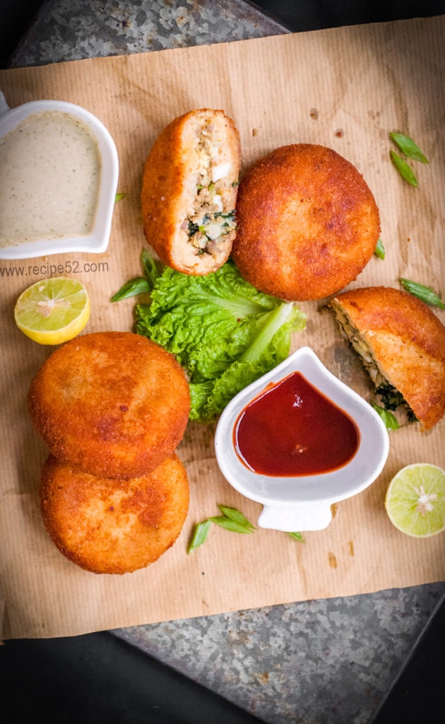 Four aloo keema patties or cutlets on a brown paper with chutney and ketchup, lemon wedges and salad leaf on the side.