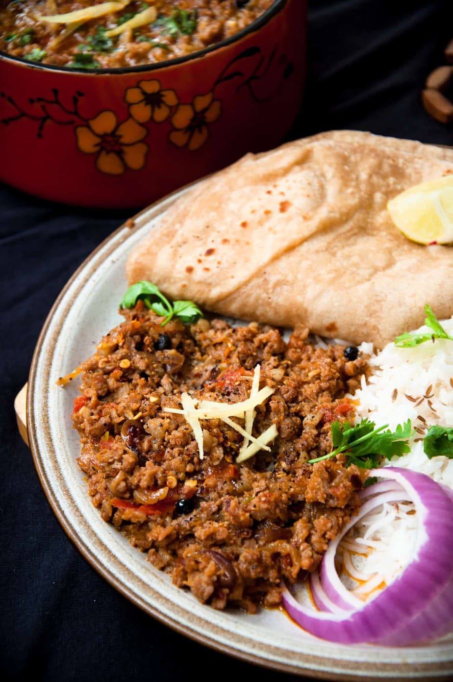 Keema served in a plate with onion slices, roti and rice. Ginger is used to garnish.