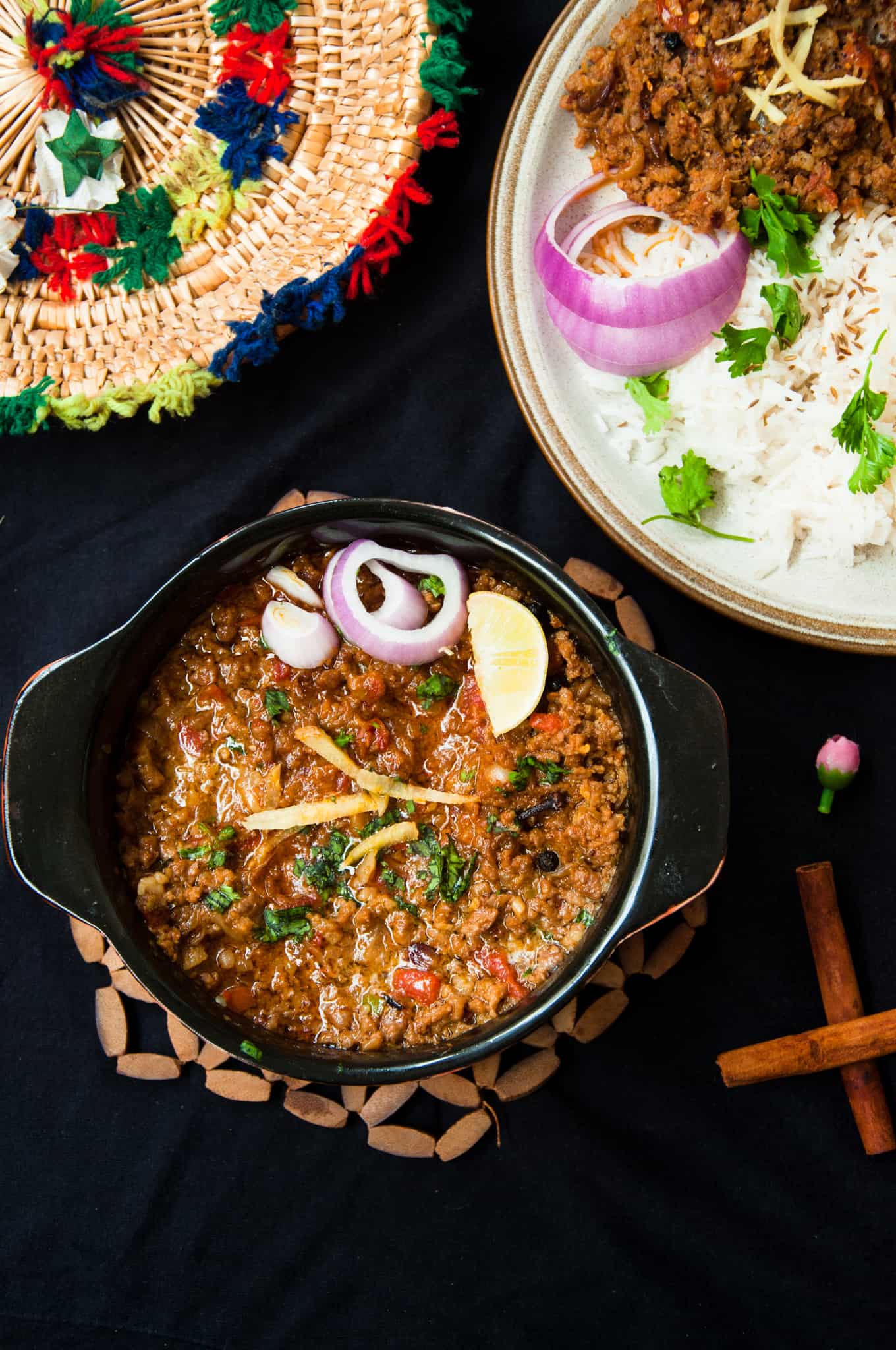 Pakistani Keema served in small black pot with onion slices and lemon wedges on the side.