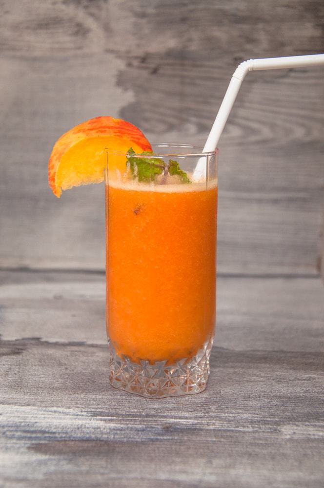 Peach juice served in a glass with slice of peach and mint leaf garnish.