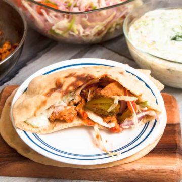 pita chicken pocket filled with chicken. Tzatziki sauce and salad bowl are in the background.