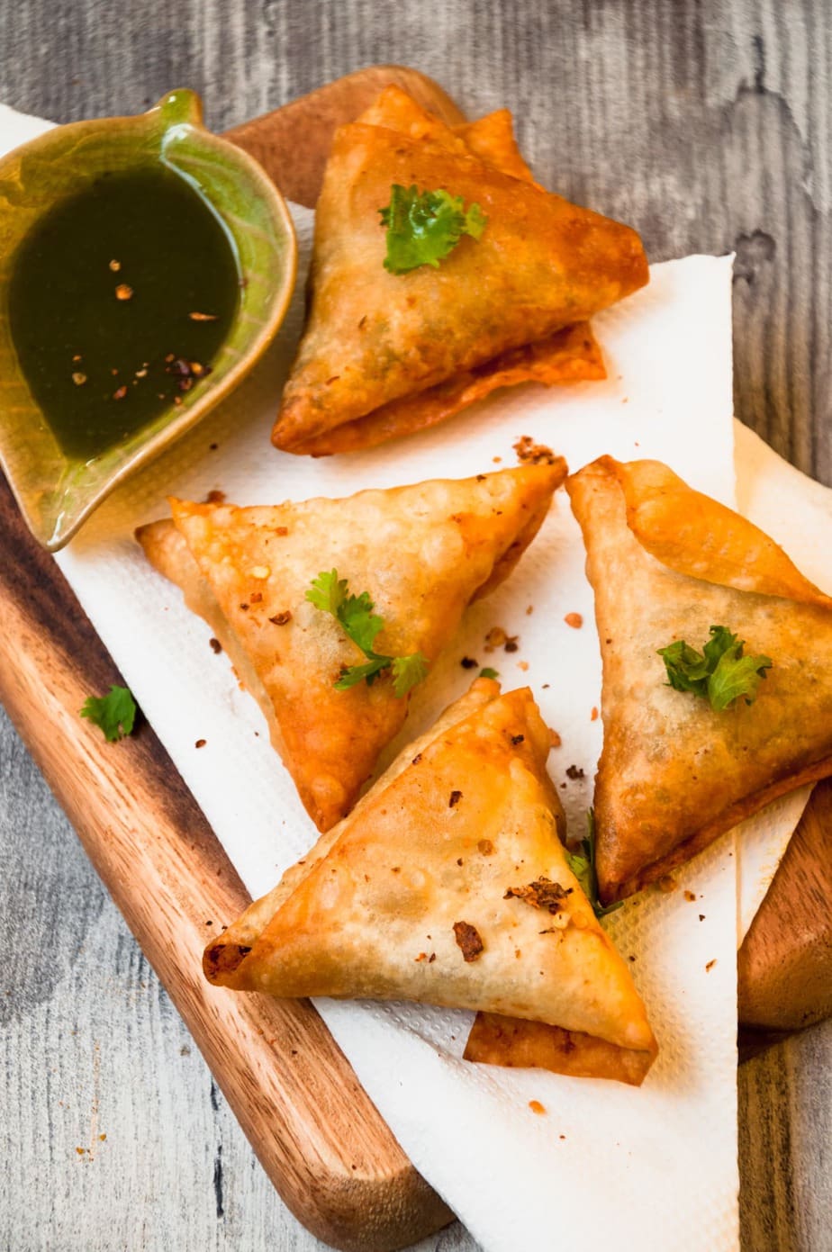 Four Samosa Triangles served in a wooden tray with green sauce on the side.