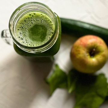 Green Spinach juice served in small jug with apple, cucumber and spinach on the side.