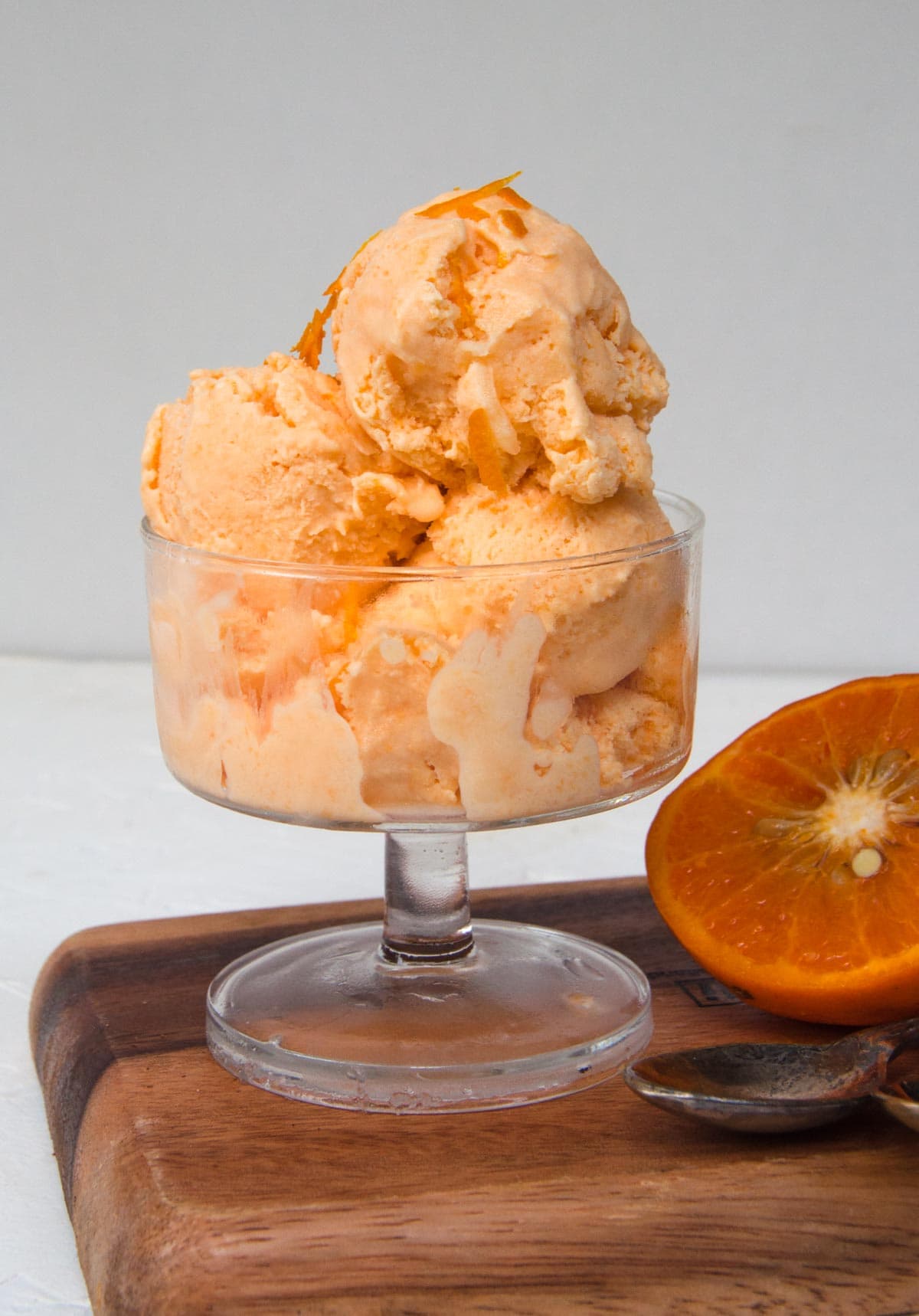 Orange ice ream scoop served in glass cup with orange on the side.