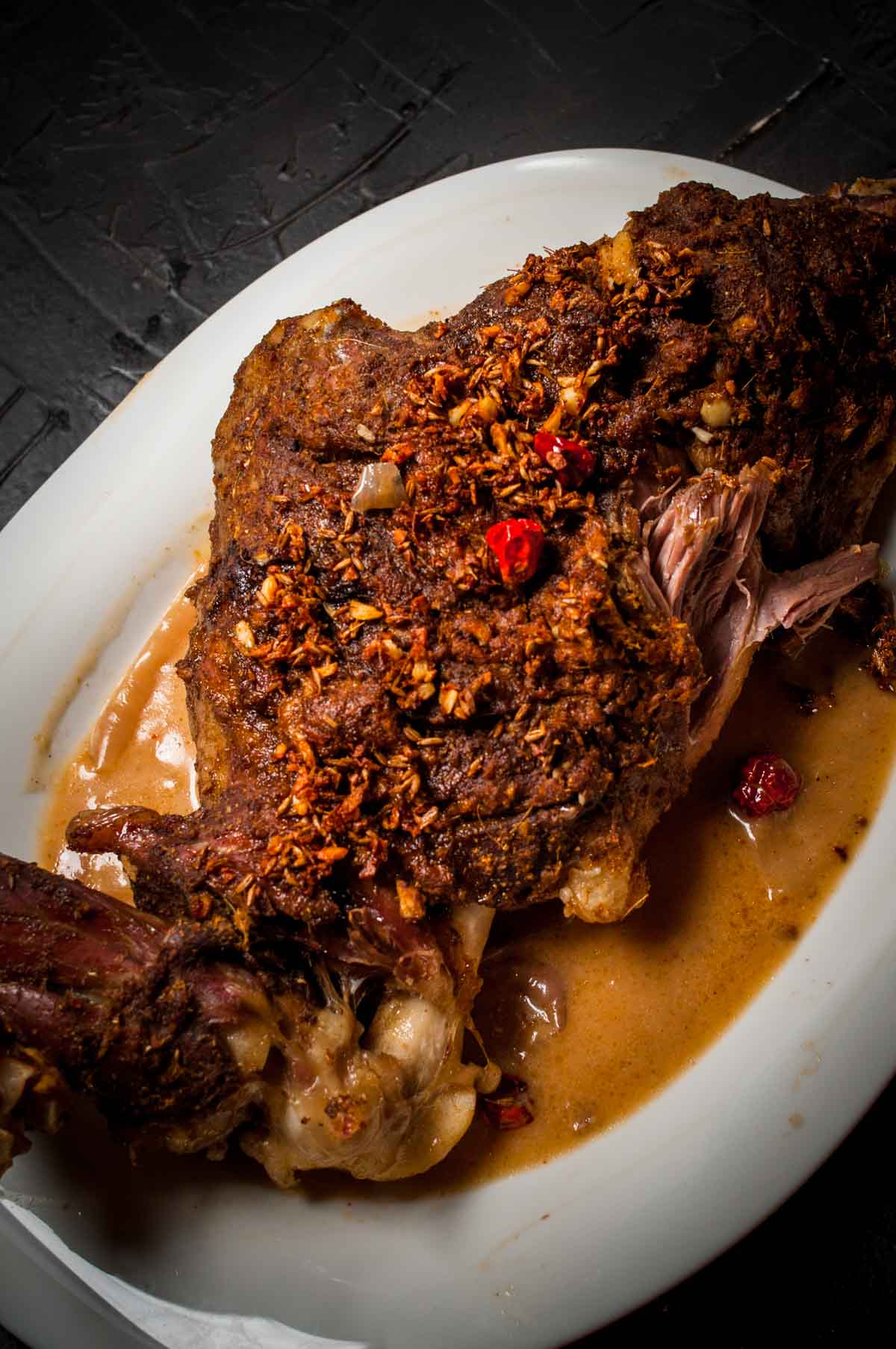 Mutton raan served in a plate over  black background.
