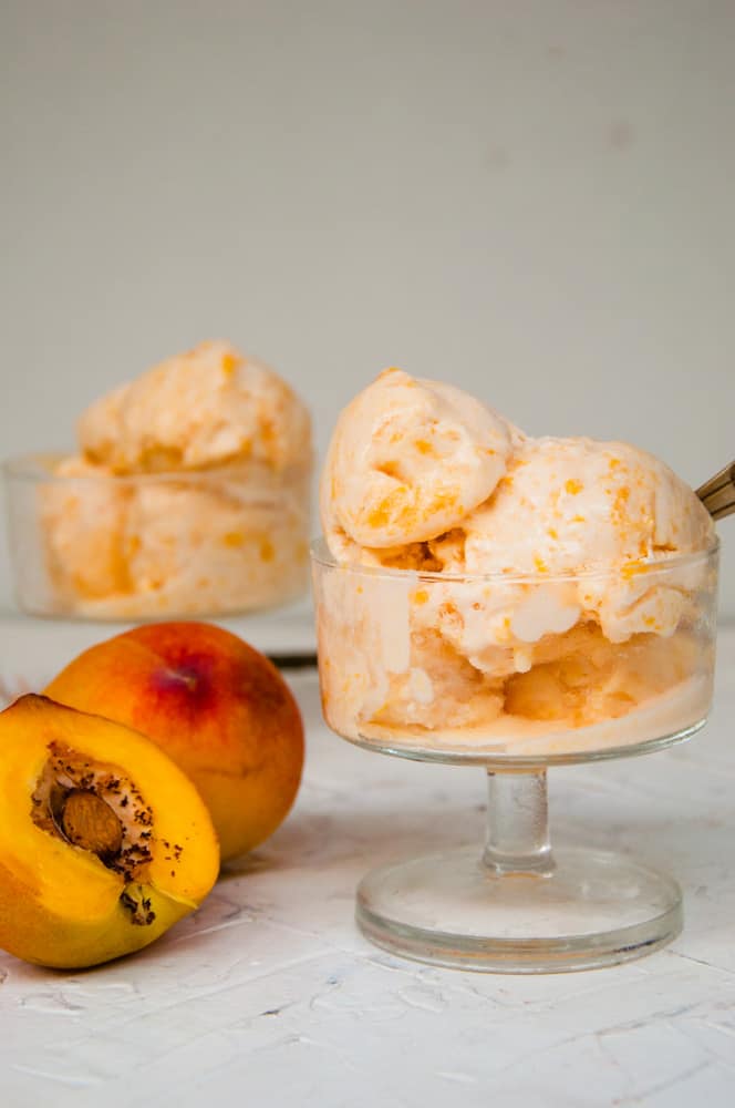 Two peach ice cream cups with a peach half in the background.