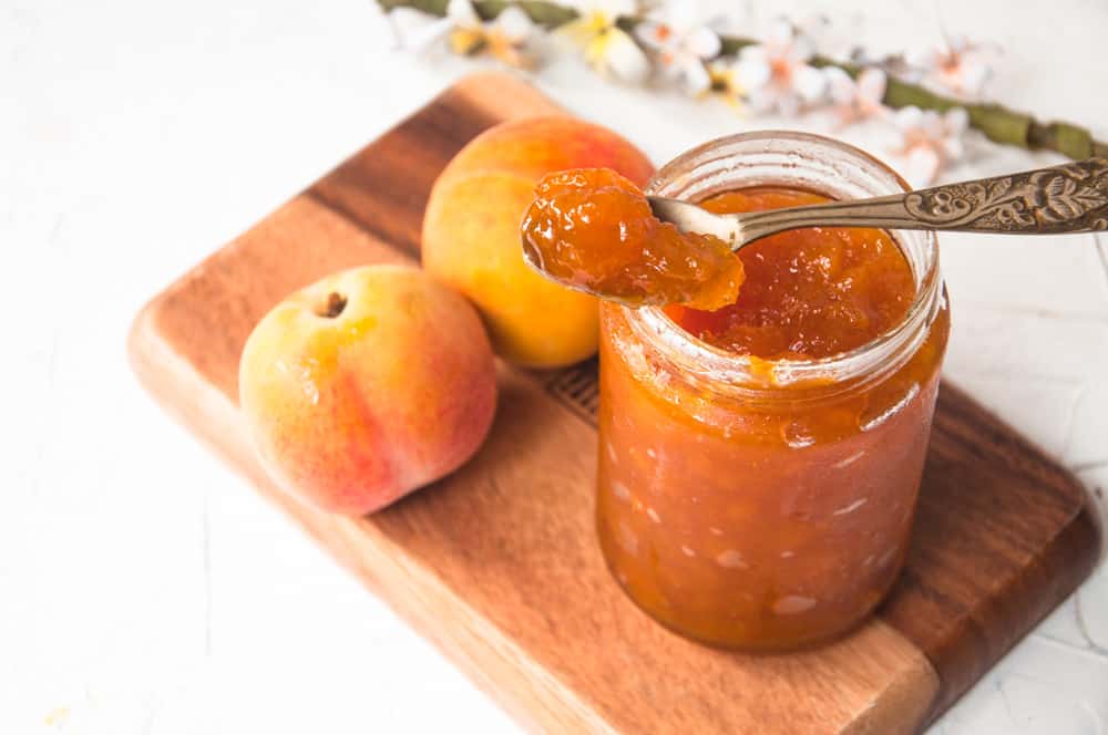 peach jam in a jar with peaches in the background.