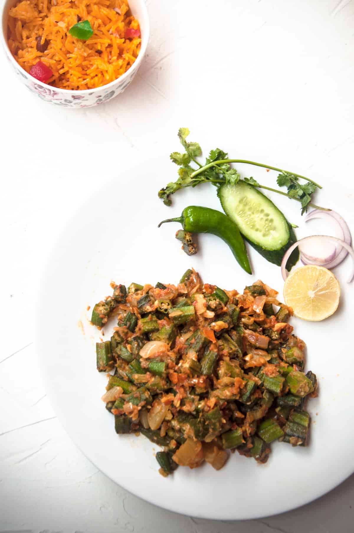 Bhindi masala served in a white plate with fresh sala and zarda in the background.