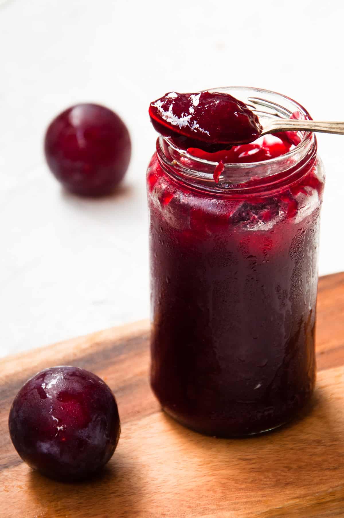 A jar of plum jam with a spoon full of jam placed on the rim.