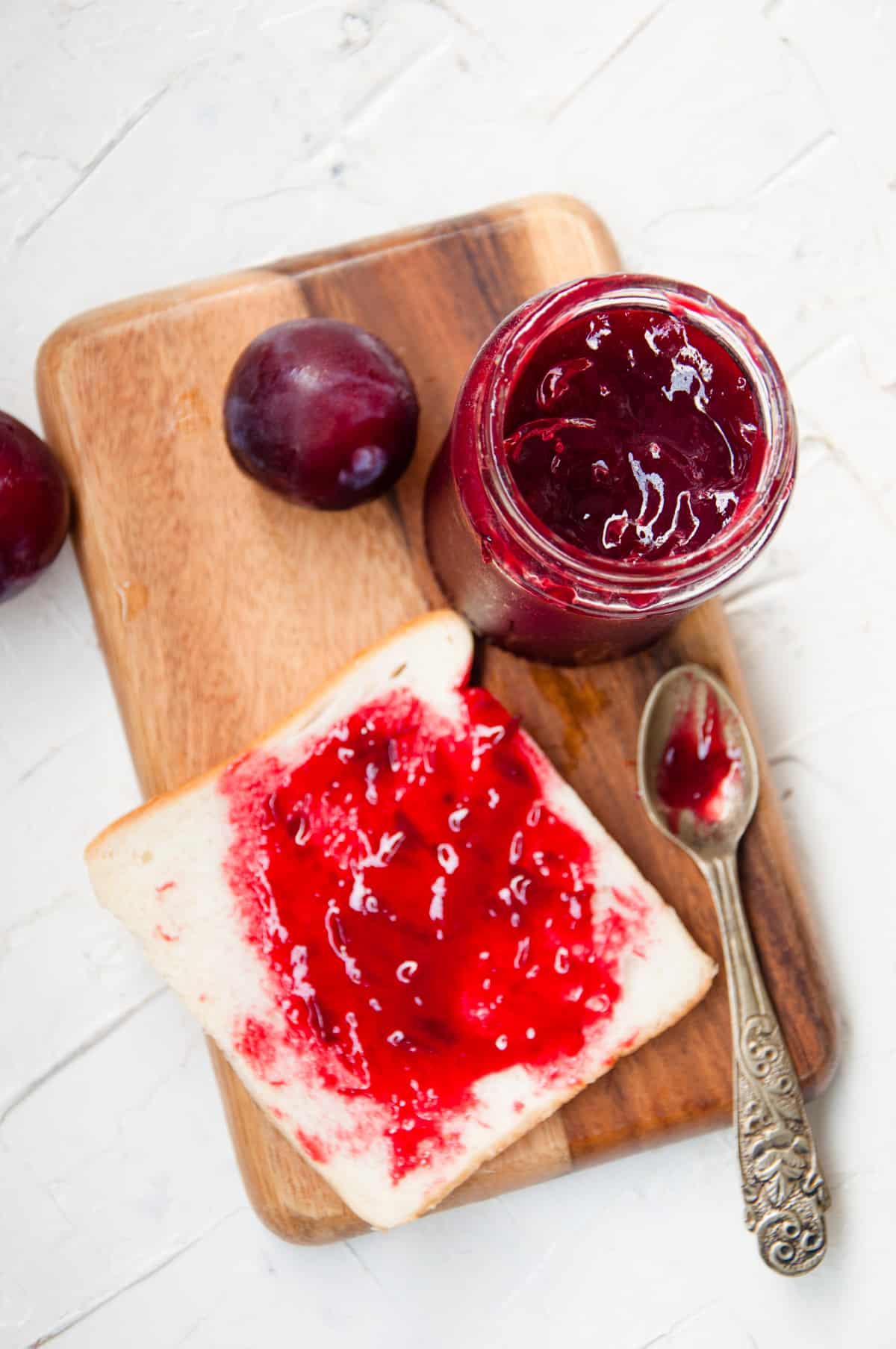 Plum jam in a jar with some jam spread on a slice of bread.
