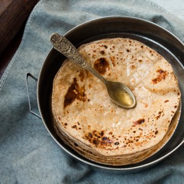 A pile of roti with spoon full of oil on it.