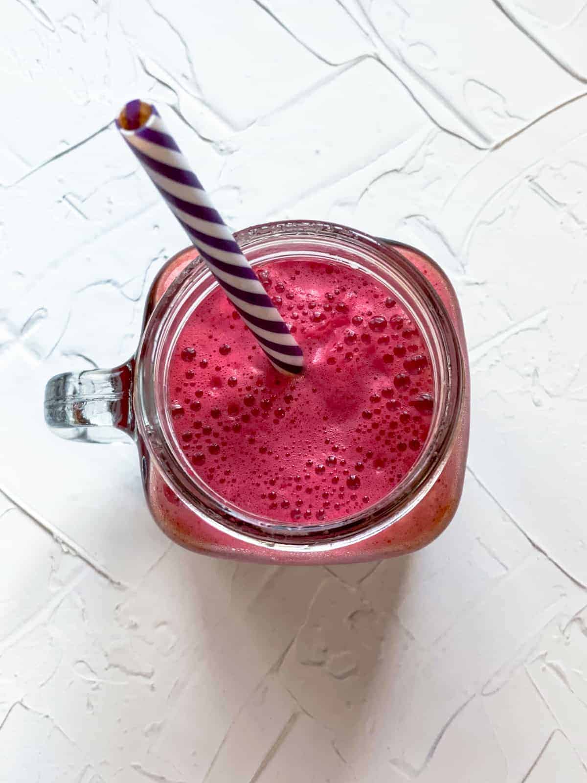 Apple beet carrot juice in a jug with straw.