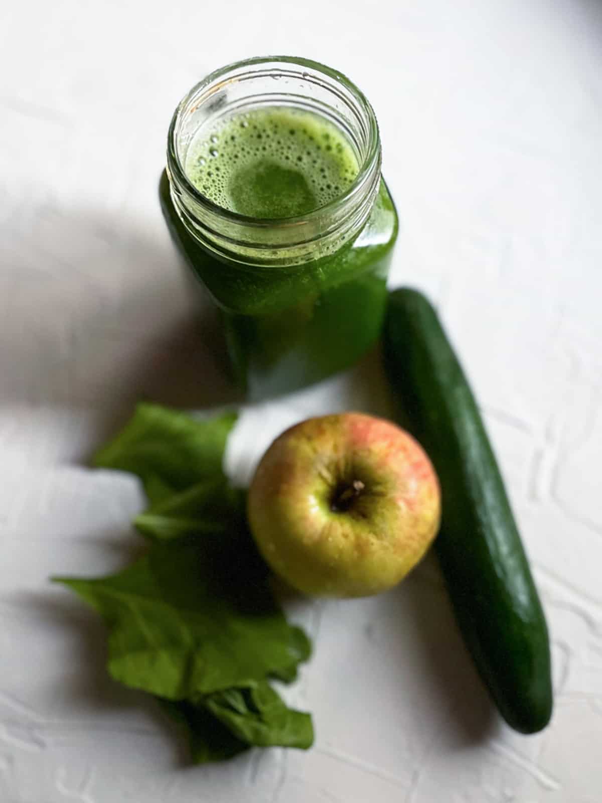 Spinach juice with spinach apple and cucumber on the fore background.