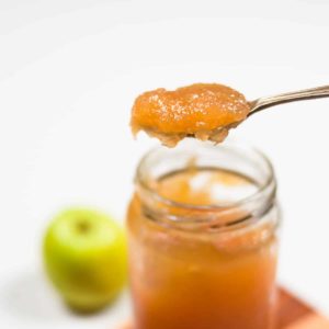 A small batch of jam in a jar with green apple in the background.