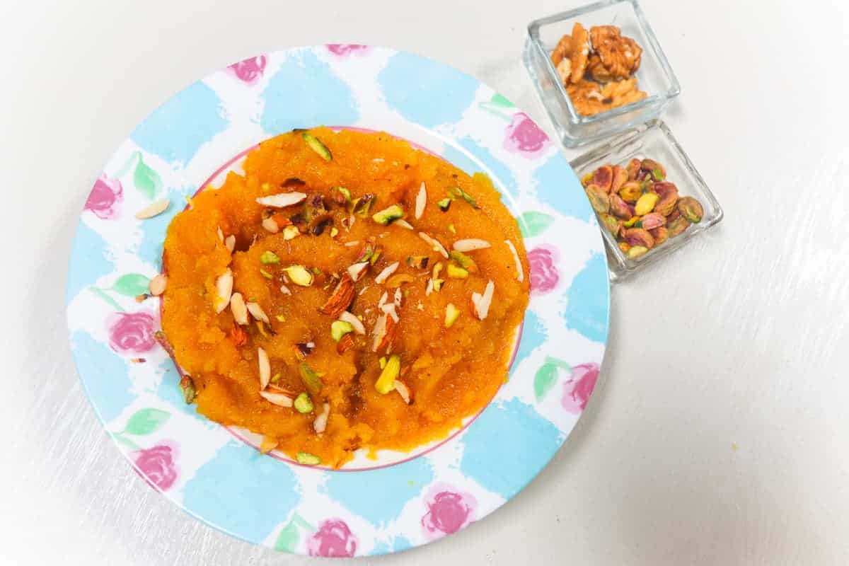 Pakistani yellow sooji halwa in the plate with nuts garnish.