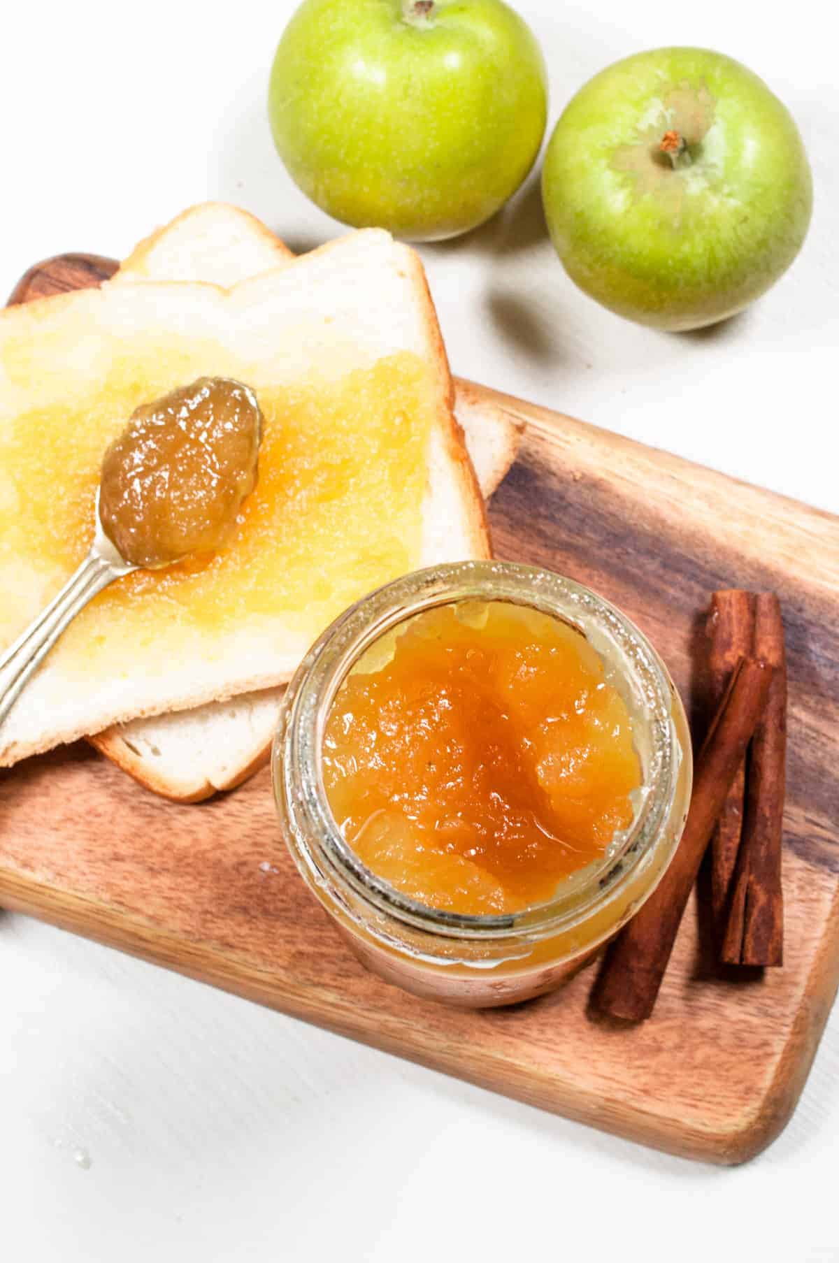 Small jar of jam with cinnamon on the side and green apples in the background.