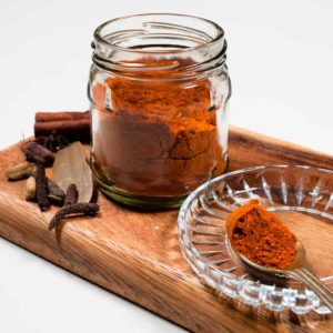 Nihari masal in a glass jar with whole spice in the back ground.