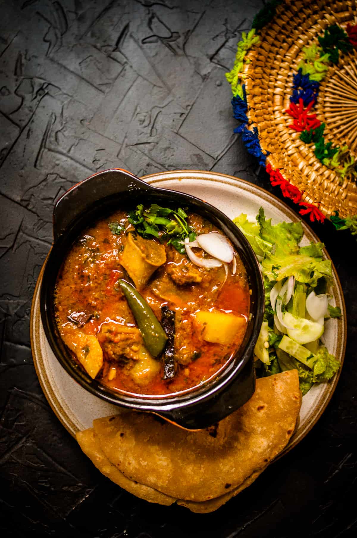 Aloo gosht served in a small clay pot with roti and salad on the side.