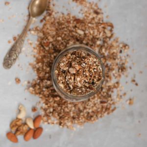 A jar of granola with spoon and nuts on the side.