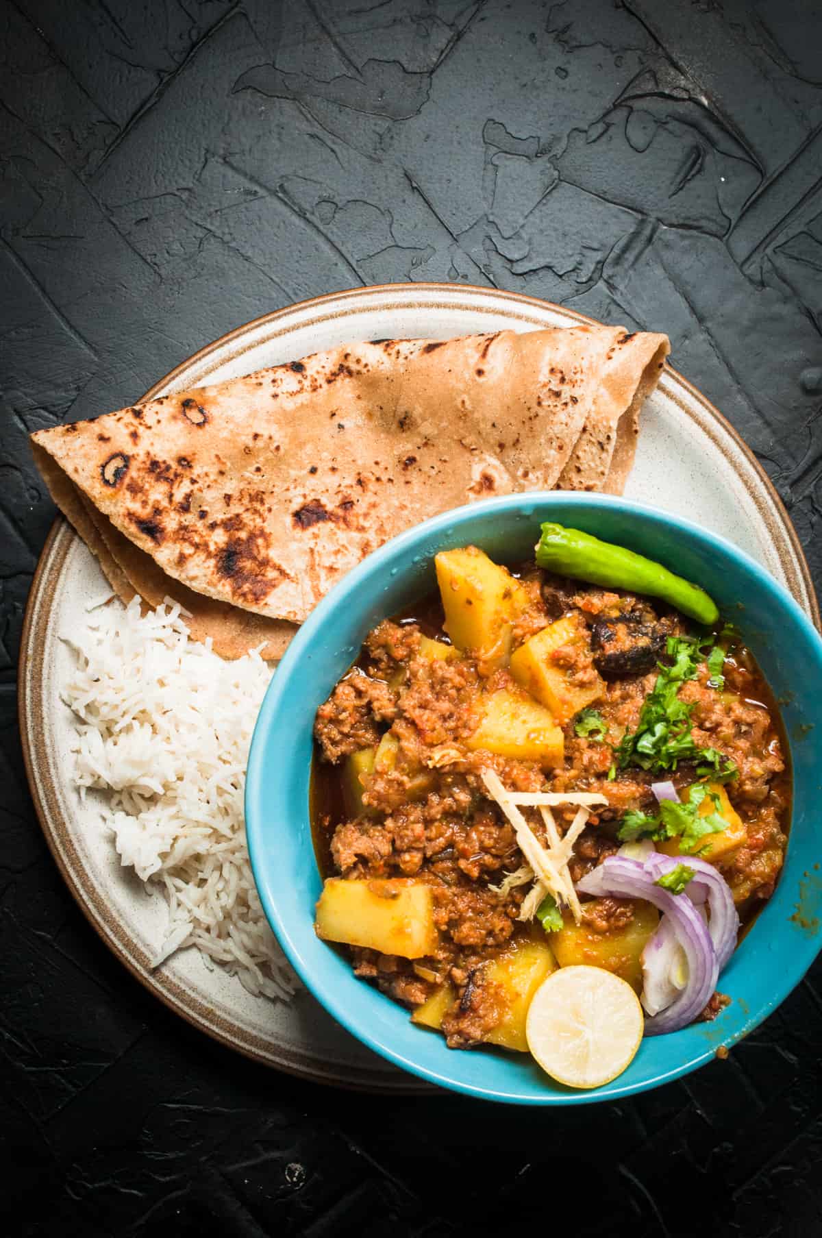 Aloo keema served in bowl with roti and rice on the side.