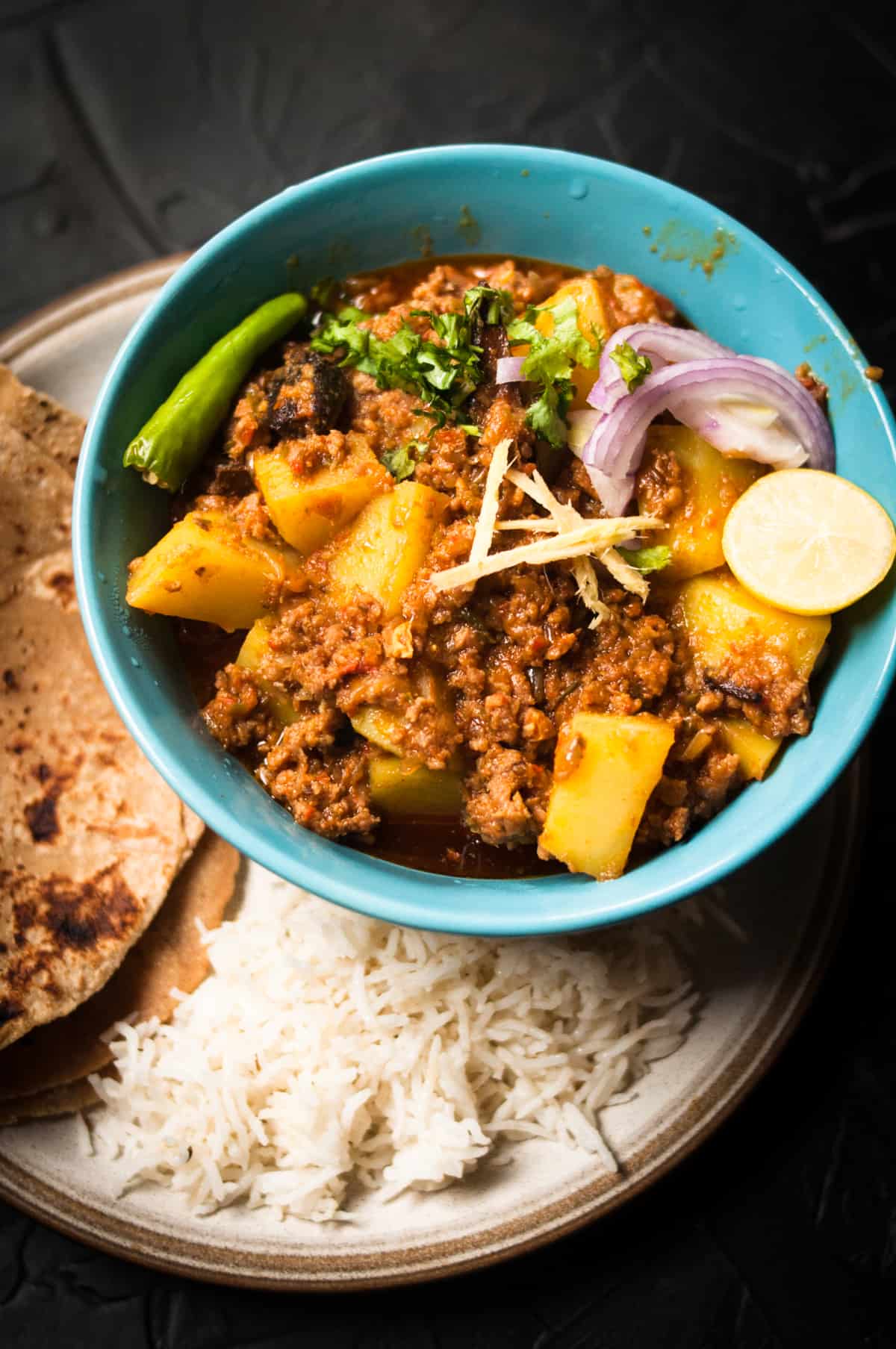 Aloo keema served served in a blue bowl over a black background.