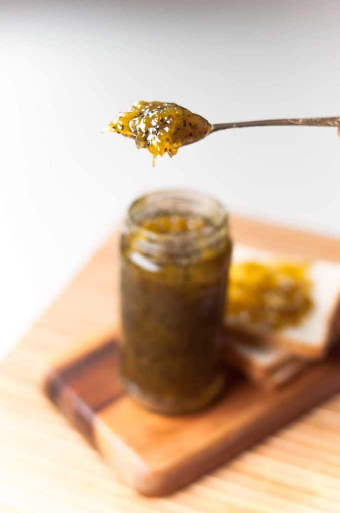 Delicious kiwi jam in the spoon with a jar of jam and a slice of bread in the background.