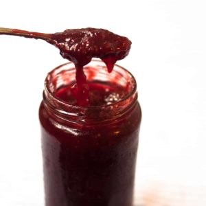 A close up shot of a spoon full strawberry jam with jam overflowing back in the jar.