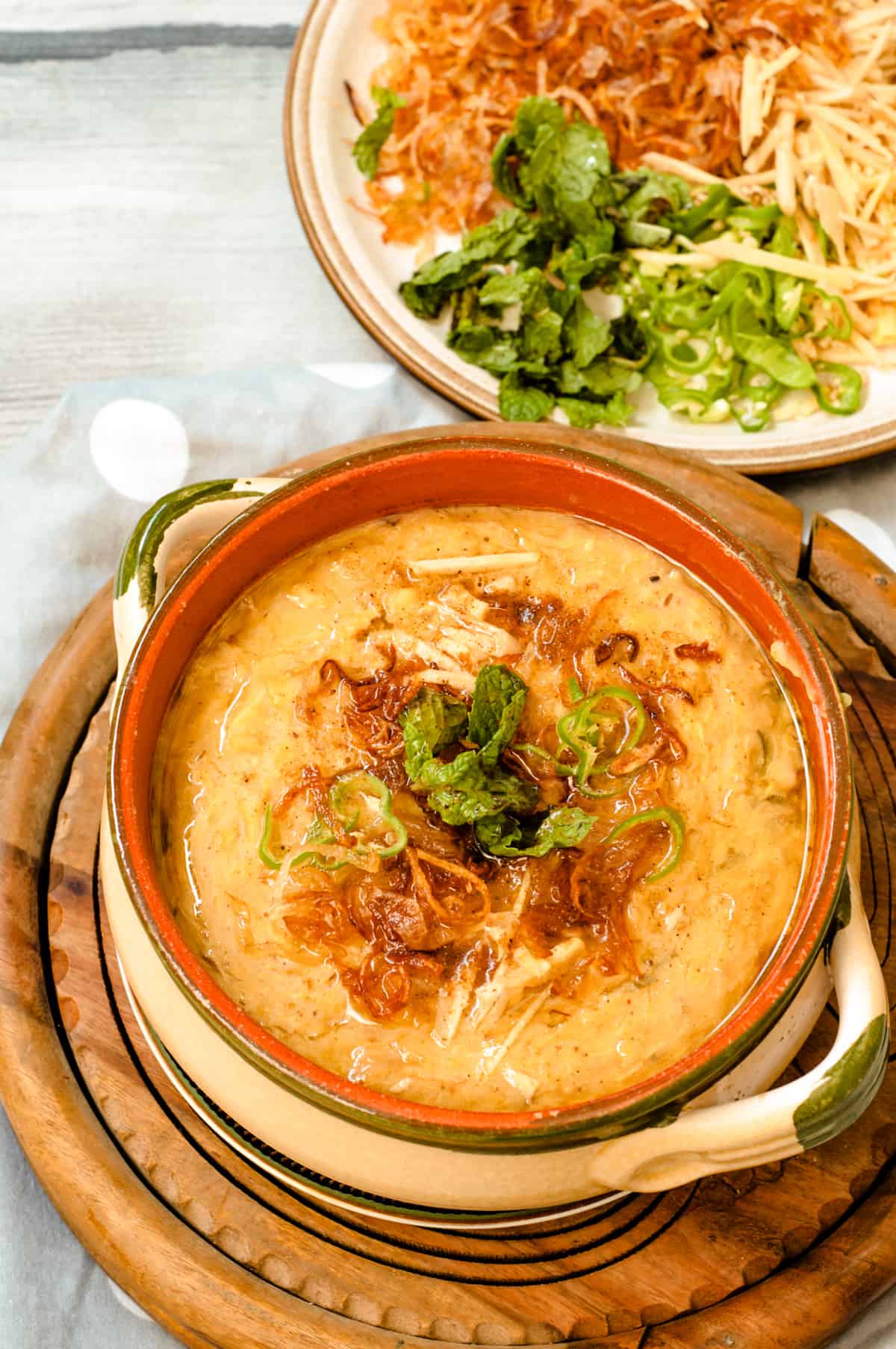 Chicken haleem served in a chay pot with garnish. Accompainment visible in the background.