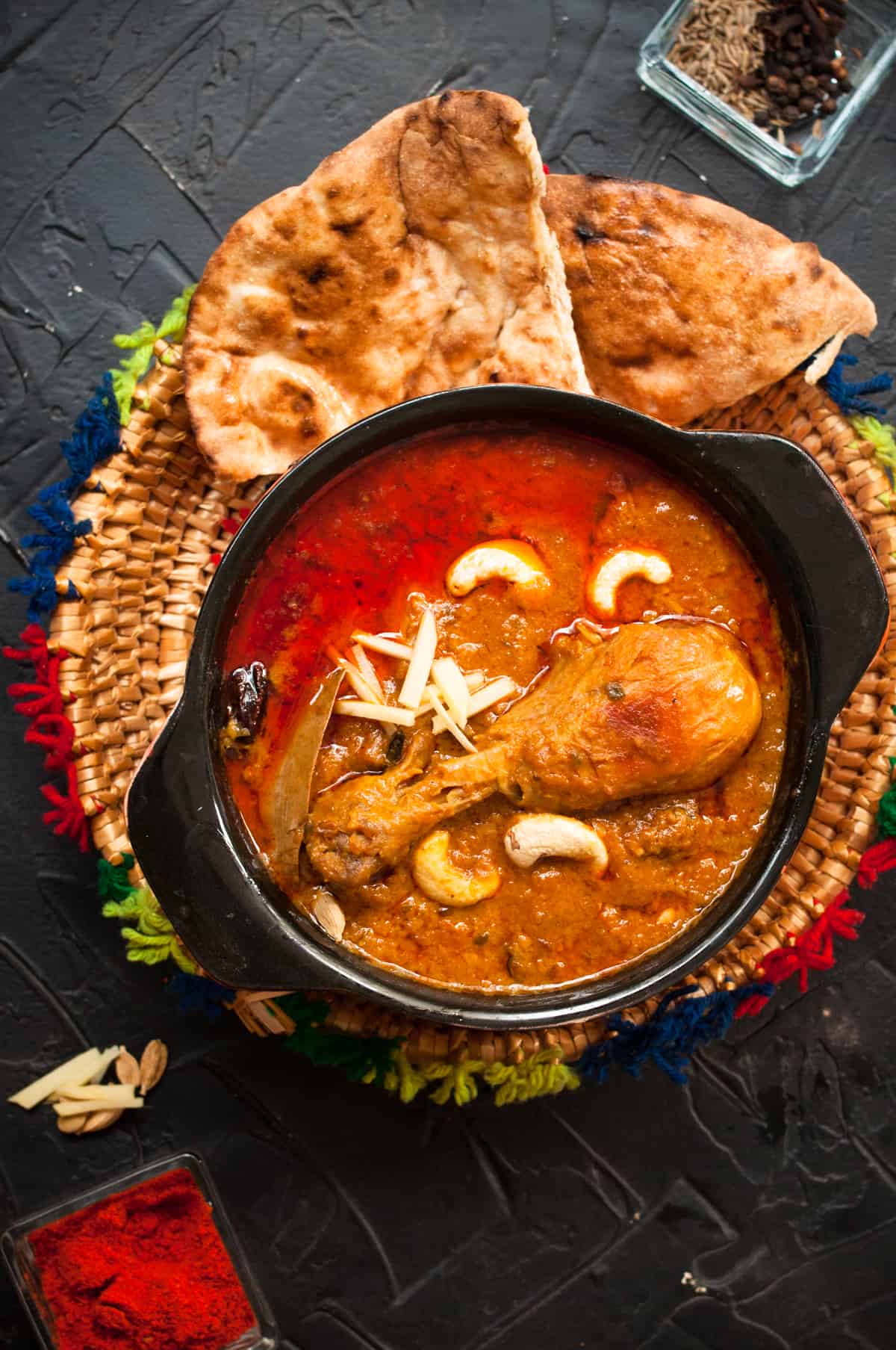 Chicken in black serving pot with taftaan and sheermal on the side.