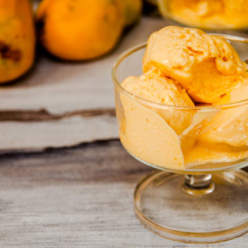 mango Ice cream served in a cup with mangoes in the background.