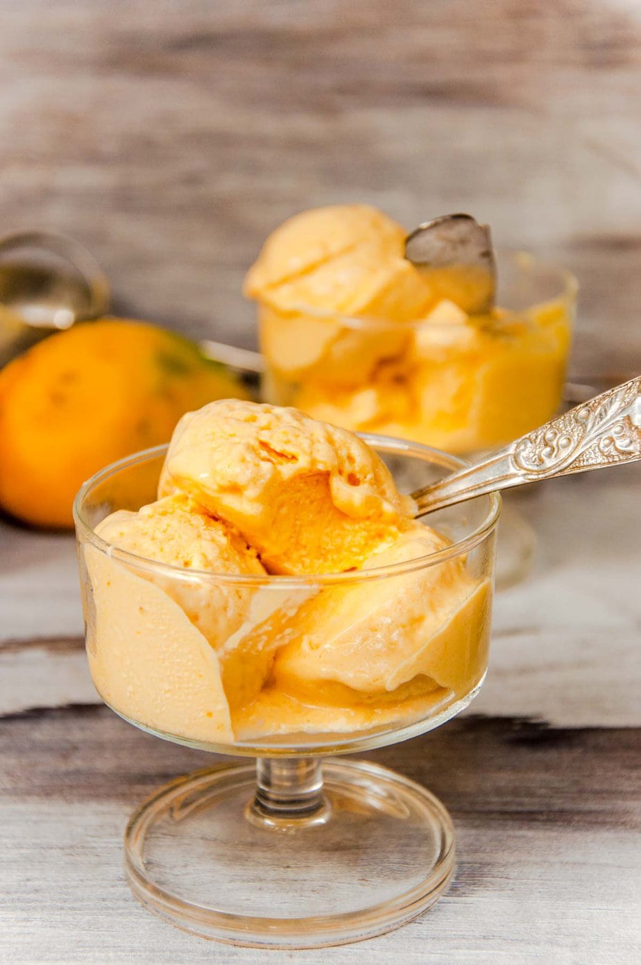 Mango ice cream scoops served in a glass ice cream cup.